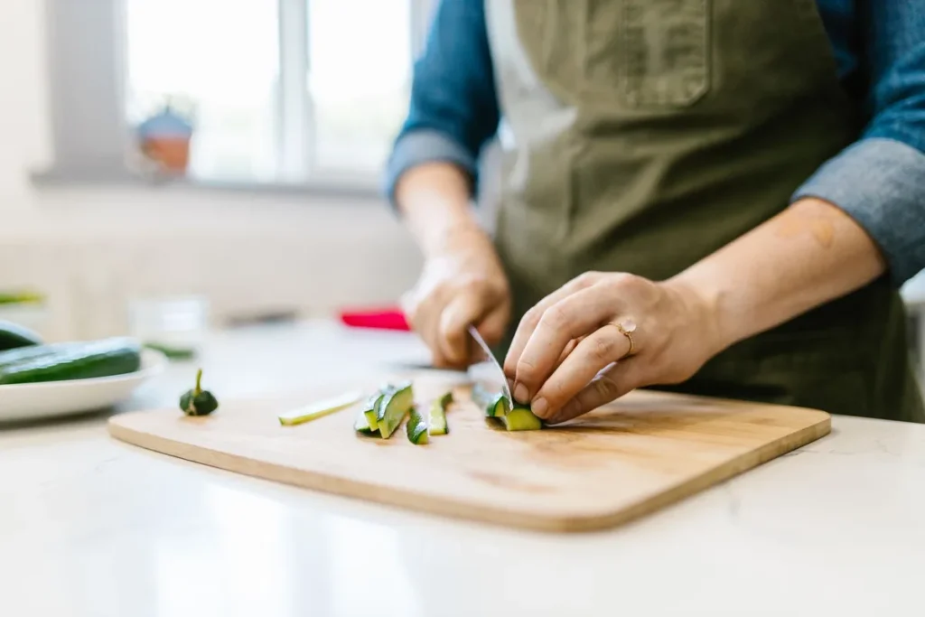 Mains préparant des courgettes fraîches sur une planche avec bocaux et balance de cuisine