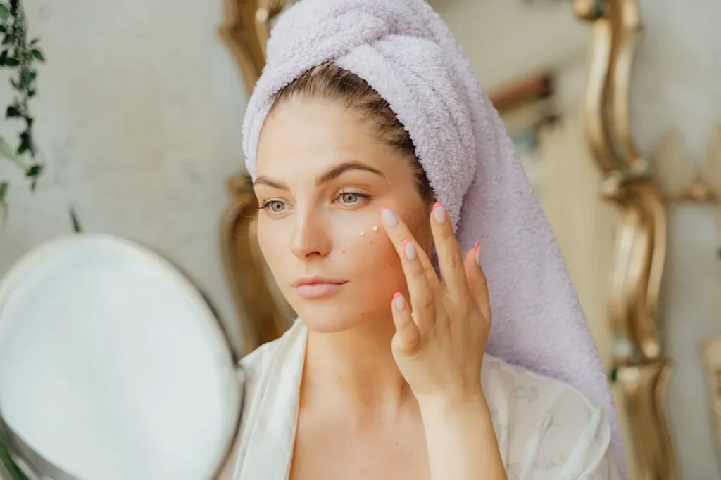Mains appliquant un soin riche blanc et crémeux sur une peau apaisée, lumière naturelle douce.