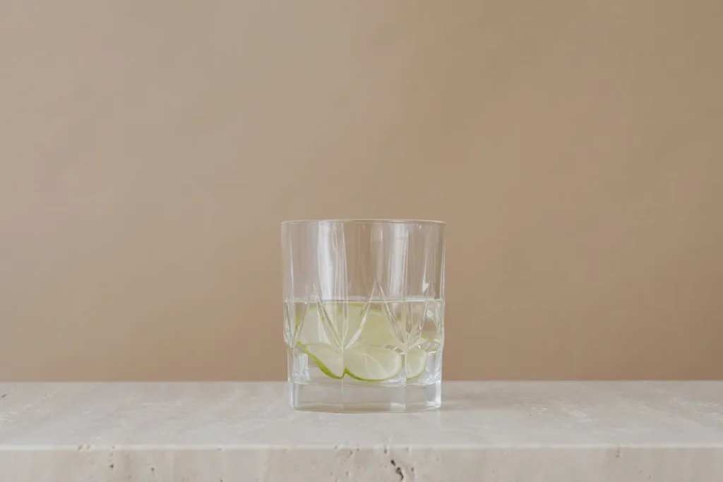 Verre transparent avec poudre de collagène dissous dans un liquide, entouré de fruits frais et d'une cuillère en bois