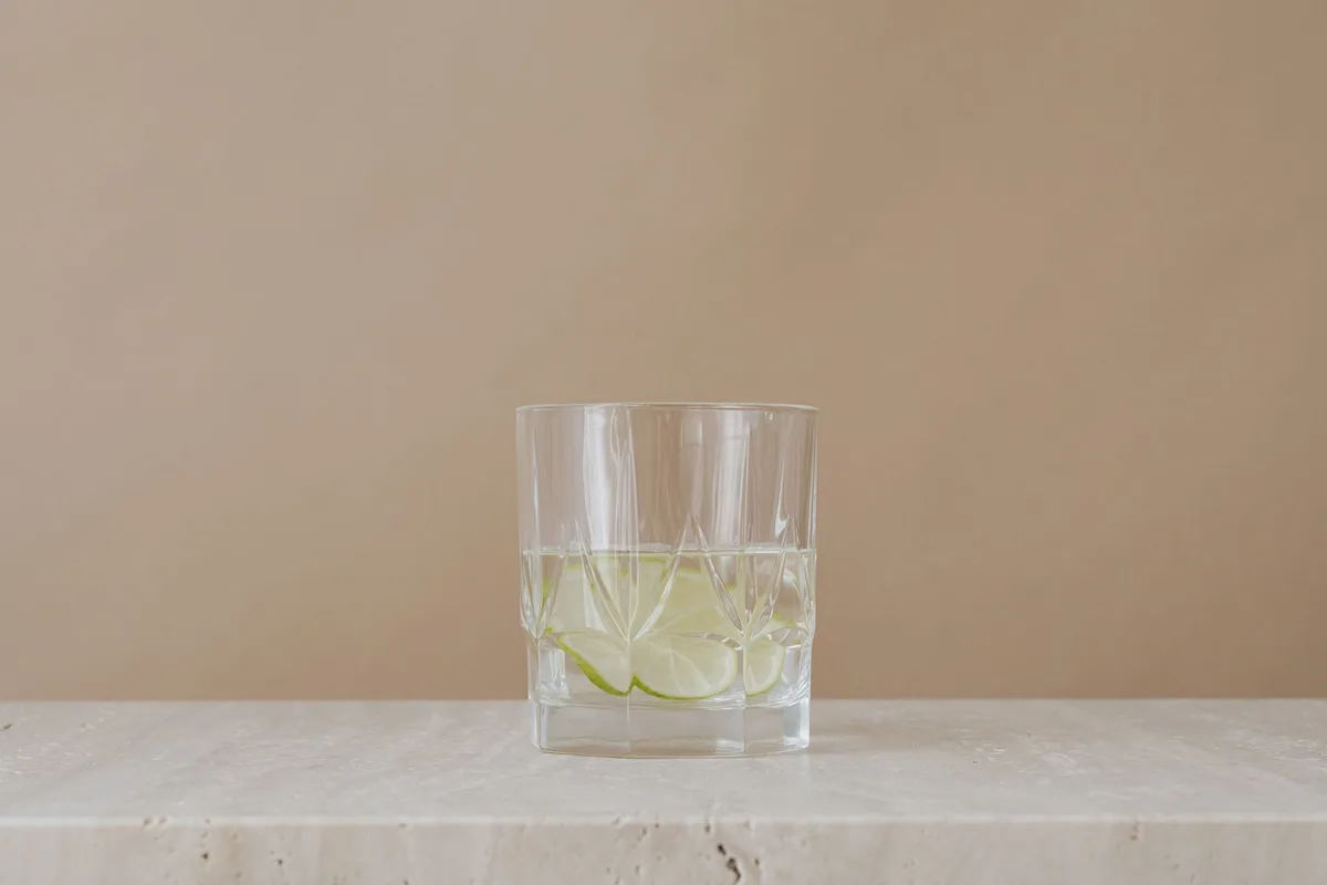 Verre transparent avec poudre de collagène dissous dans un liquide, entouré de fruits frais et d'une cuillère en bois