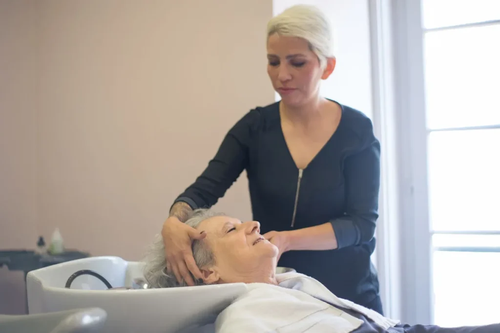 Mains massant délicatement le cuir chevelu sous l'eau tiède avec mousse de shampooing