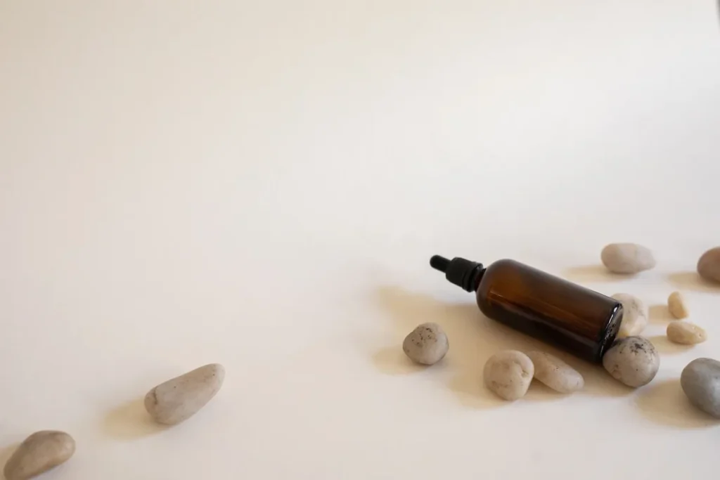 Petite bouteille d'huile capillaire posée sur une serviette de plage ensoleillée avec des gouttes d'eau scintillantes