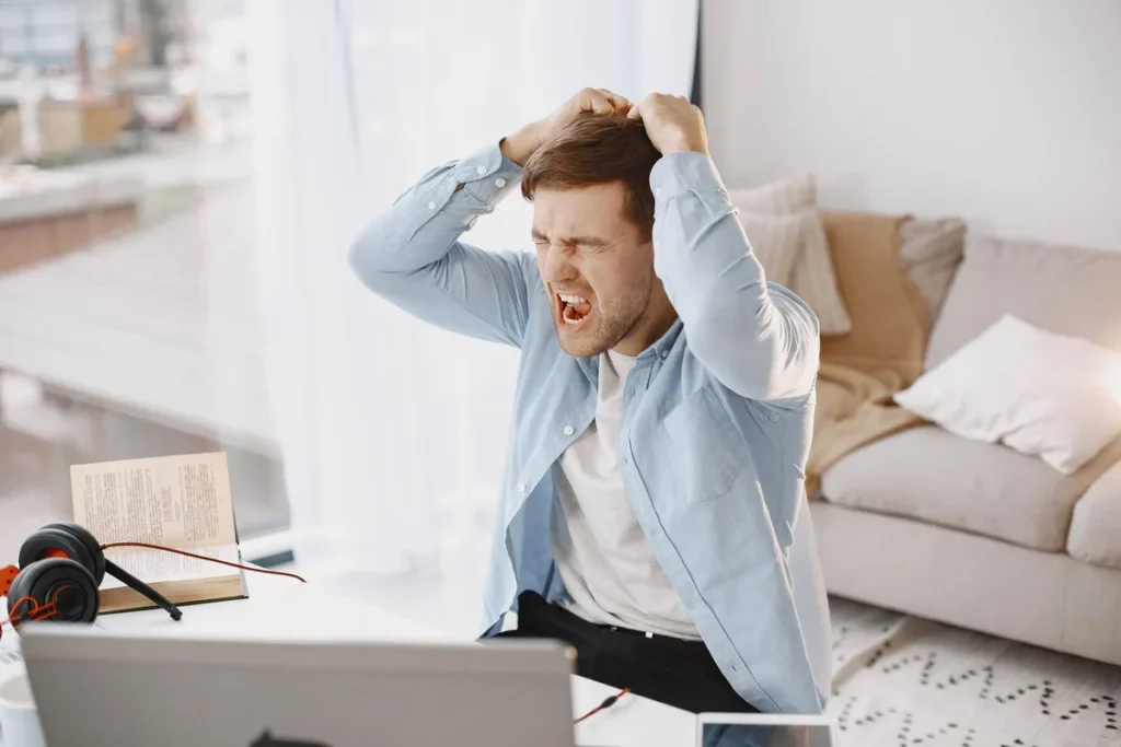 Personne assise à un bureau, main sur le front, exprimant la frustration et le stress au travail