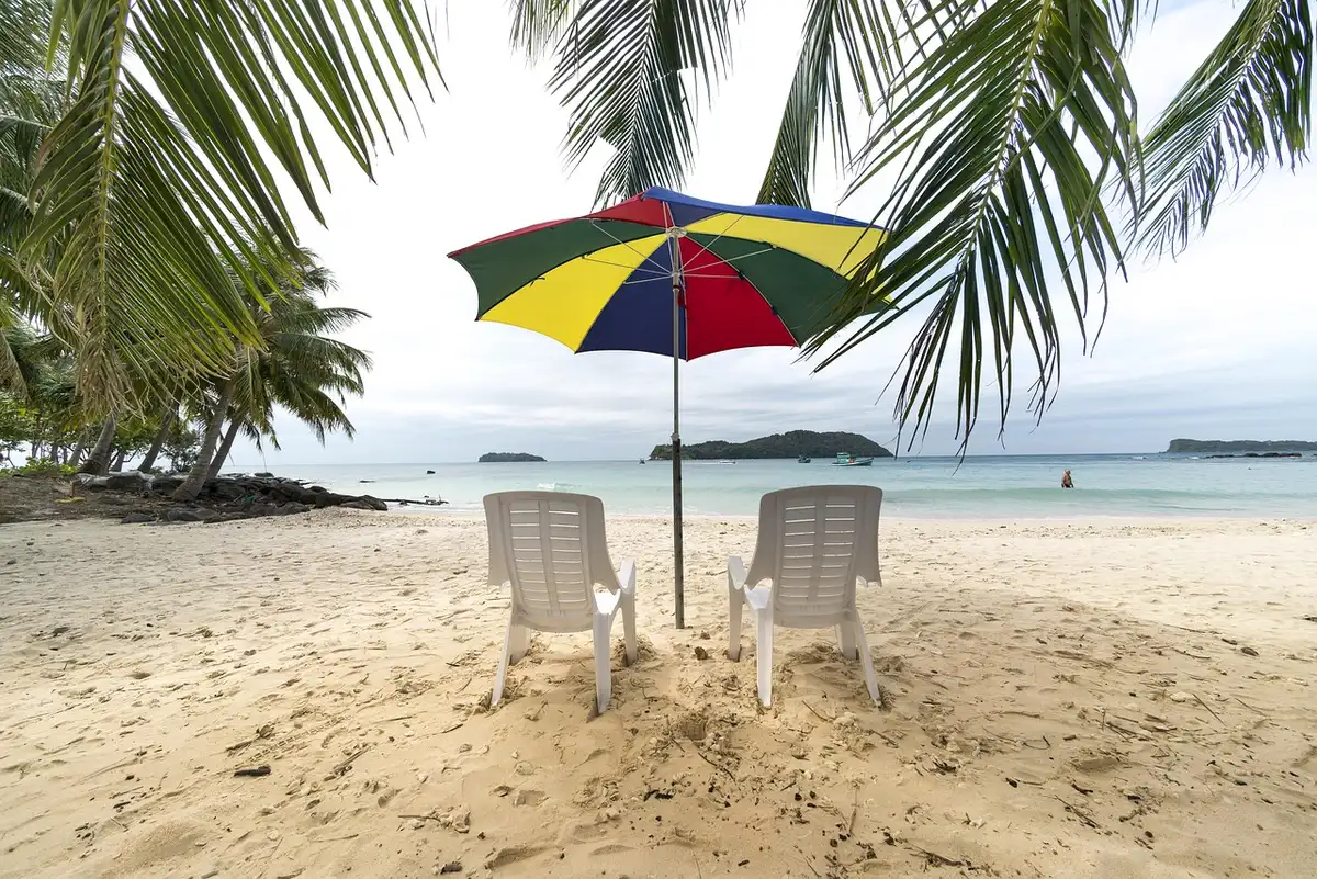 Parasol sur la plage projetant une ombre sur le sable, avec lumière diffuse et reflets de l'eau